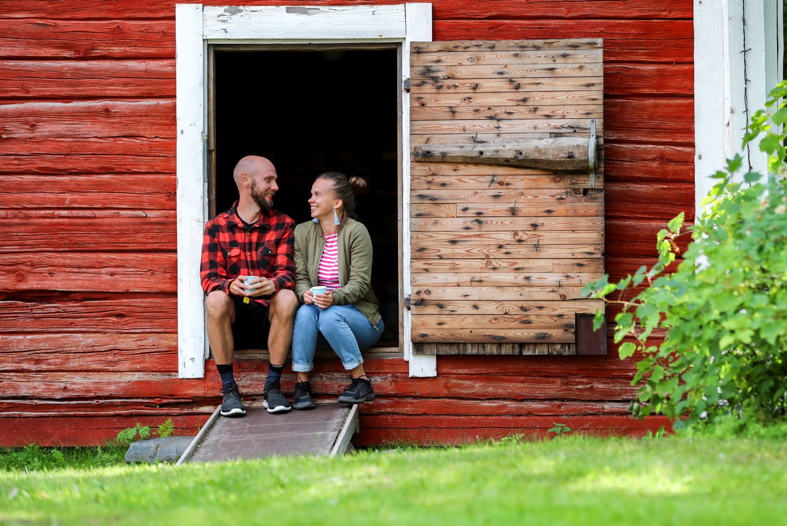 Mies ja nainen istuvat vanhan aitan oven kynnyksellä katsoen toisiaan.